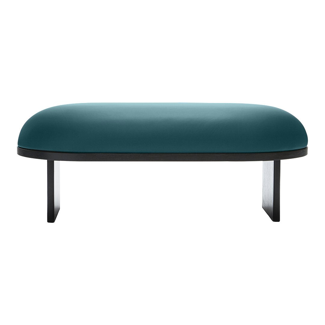 Teal velvet ottoman with a smooth, rounded surface and sleek black legs, showcasing a modern minimalist design.