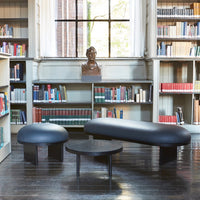 Black curved bench and table set on dark hardwood floor, surrounded by a library with colorful bookshelves.