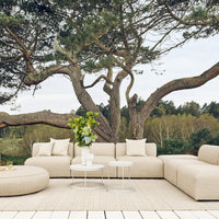 Beige outdoor sectional sofa with soft cushions, paired with a round ottoman and minimalistic white tables.