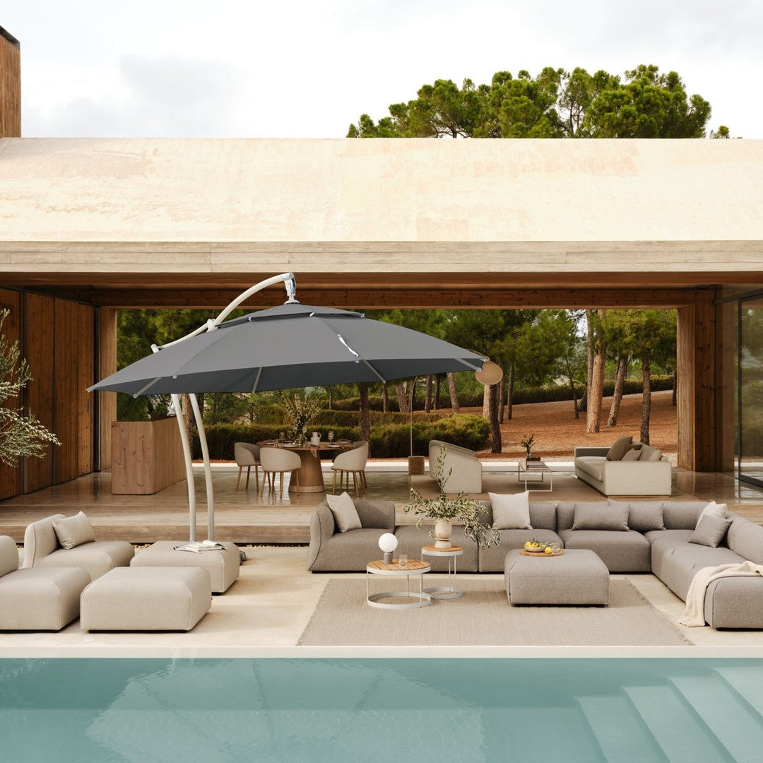 Gray umbrella over modern beige patio furniture by a pool, surrounded by green trees and natural wood accents.
