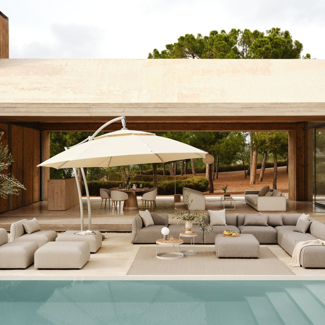 Gray and beige outdoor lounge furniture with a white umbrella, set against a serene, green landscape.