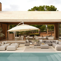 Gray and beige outdoor lounge furniture with a white umbrella, set against a serene, green landscape.