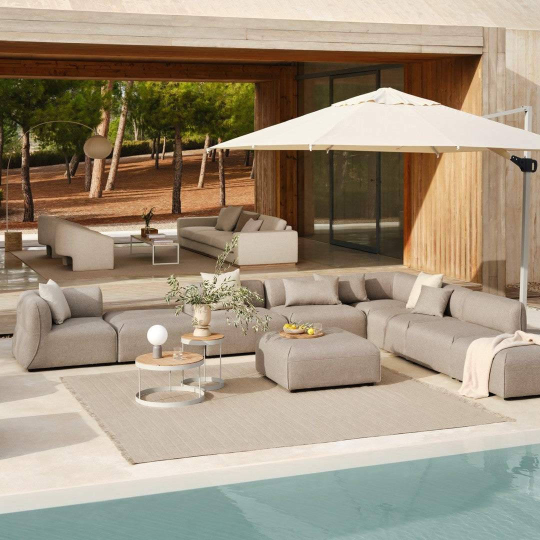 Neutral beige sectional sofa set with a light cream umbrella and textured rug by the poolside.