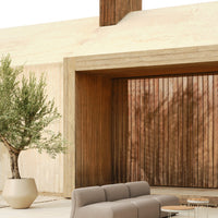 "Neutral beige walls with rich wooden paneling and soft gray outdoor seating, accented by green foliage."