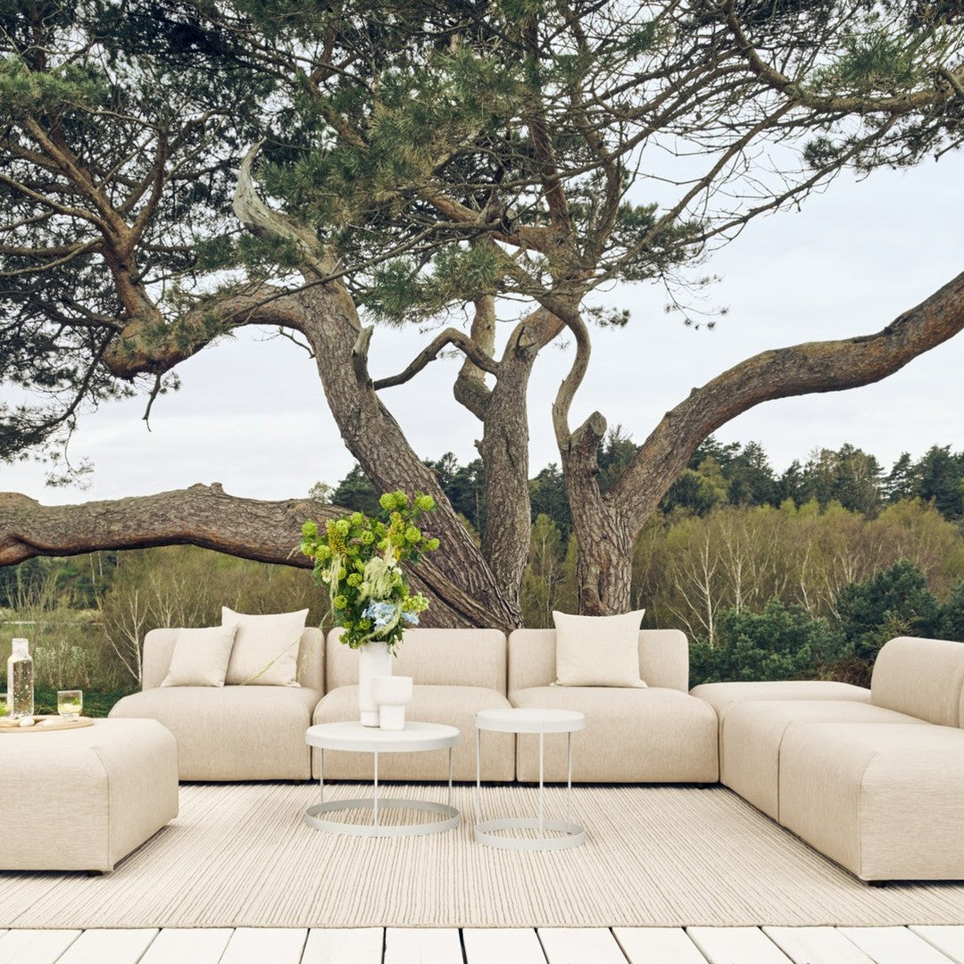 Beige modular outdoor sofa with plush cushions, set against a backdrop of greenery and natural wood tones.
