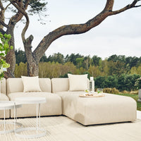 Beige sectional sofa with clean lines and soft fabric, complemented by white cushions against a natural outdoor backdrop.