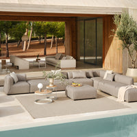"Modern outdoor sectional sofa in soft gray fabric, paired with a beige rug, set against a serene natural backdrop."