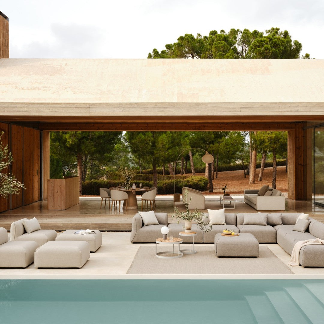 Neutral beige outdoor furniture set with soft gray accents, complemented by a serene blue pool against a natural backdrop.