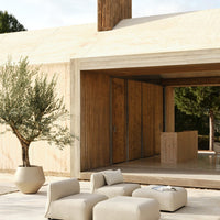 Modern neutral-colored furniture set against a natural wood and sandy background with olive greenery.