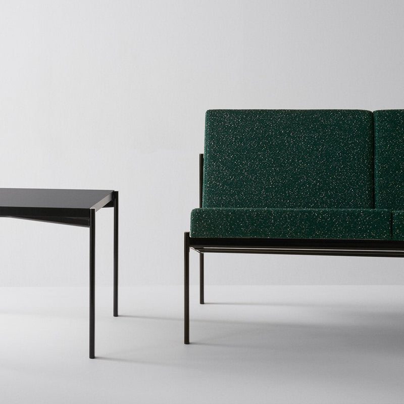 Green textured upholstery sofa with a minimalist black metal frame, paired with a sleek black table.