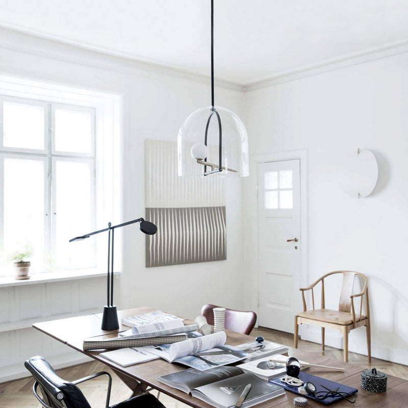 Clear glass pendant lamp with black accents, surrounded by a minimalist white and wood interior with subtle textural patterns.