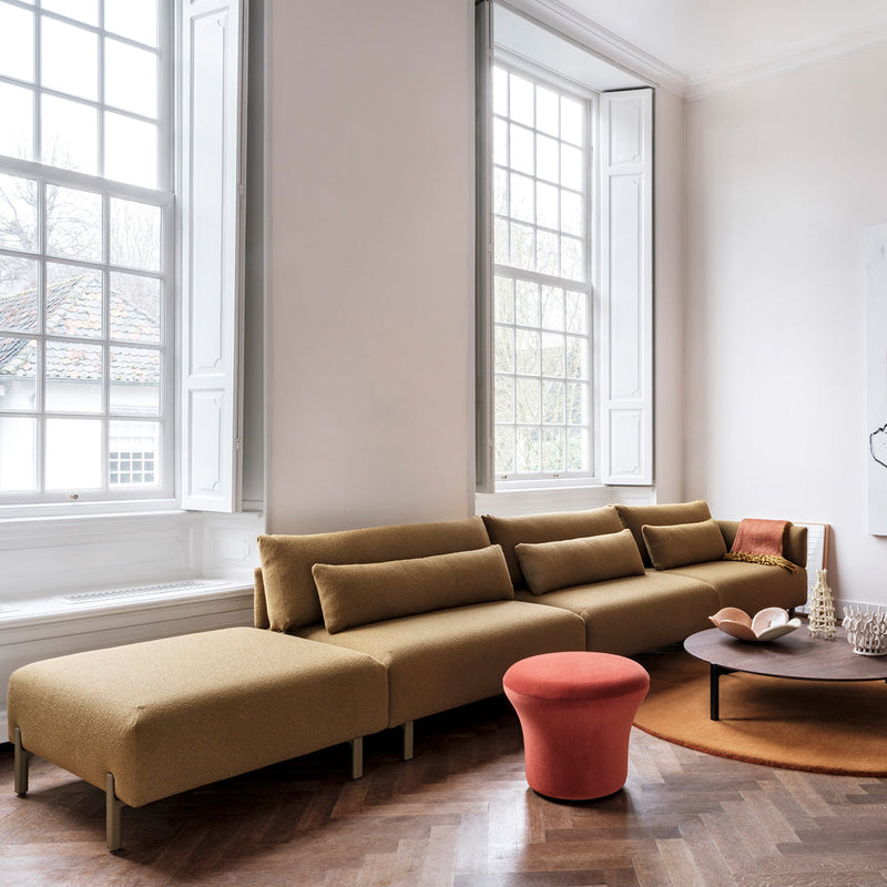 "Modern mustard sofa with sleek lines, complemented by a coral accent stool and earthy round rug."