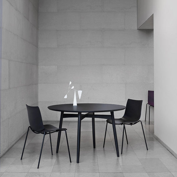 Modern round black dining table with sleek black chairs, set against a light gray minimalist backdrop.