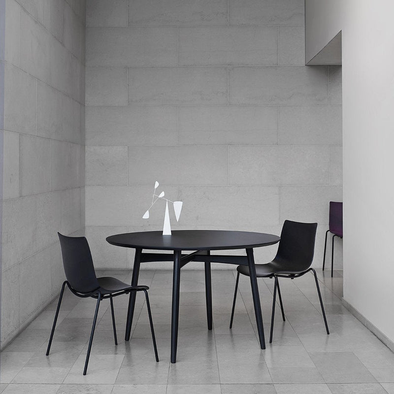 Modern round black dining table with sleek black chairs, set against a light gray minimalist backdrop.