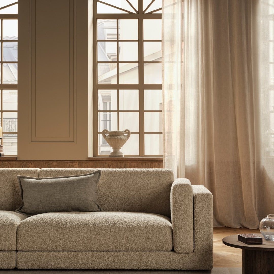 Beige textured sofa with a subtle pattern, complemented by soft light curtains and warm wooden accents.