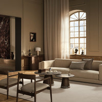 Neutral beige sofa with gray cushions, wooden chairs, and soft cream curtains against a warm brown accent wall.