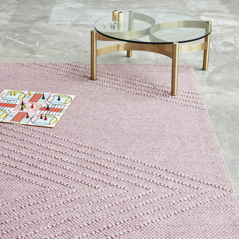 Pink textured area rug with diagonal lines and a playful pattern, complementing a modern glass coffee table.