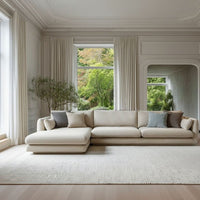 Light beige sectional sofa with soft gray and blue cushions, set against a bright, airy room with natural light.