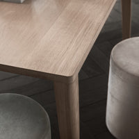 Light wood table with smooth finish, paired with soft, round, muted gray and cream velvet stools. Elegant, modern design.