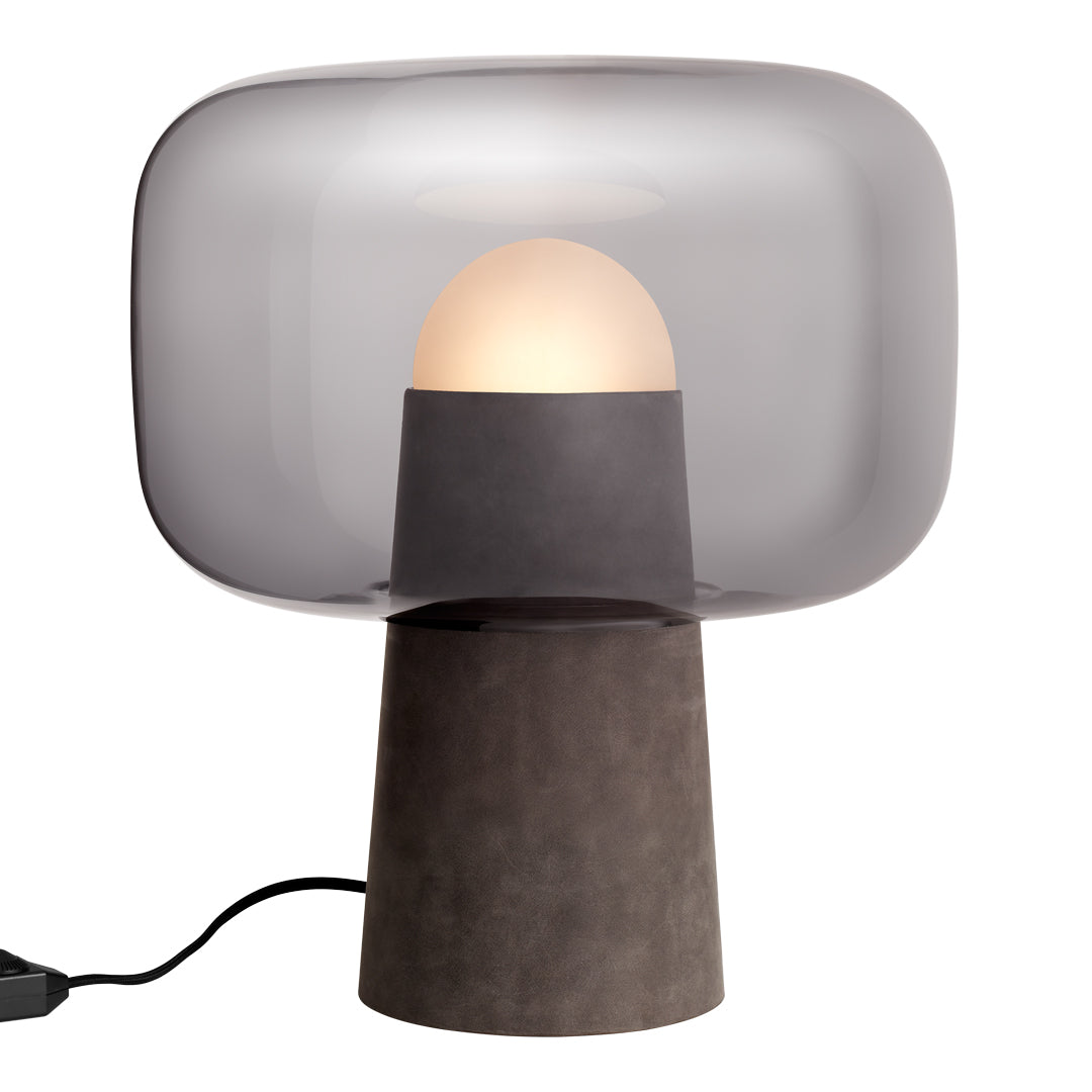 Modern table lamp with a smoky grey shade and a sleek black base. Round white bulb creates a soft, warm glow.