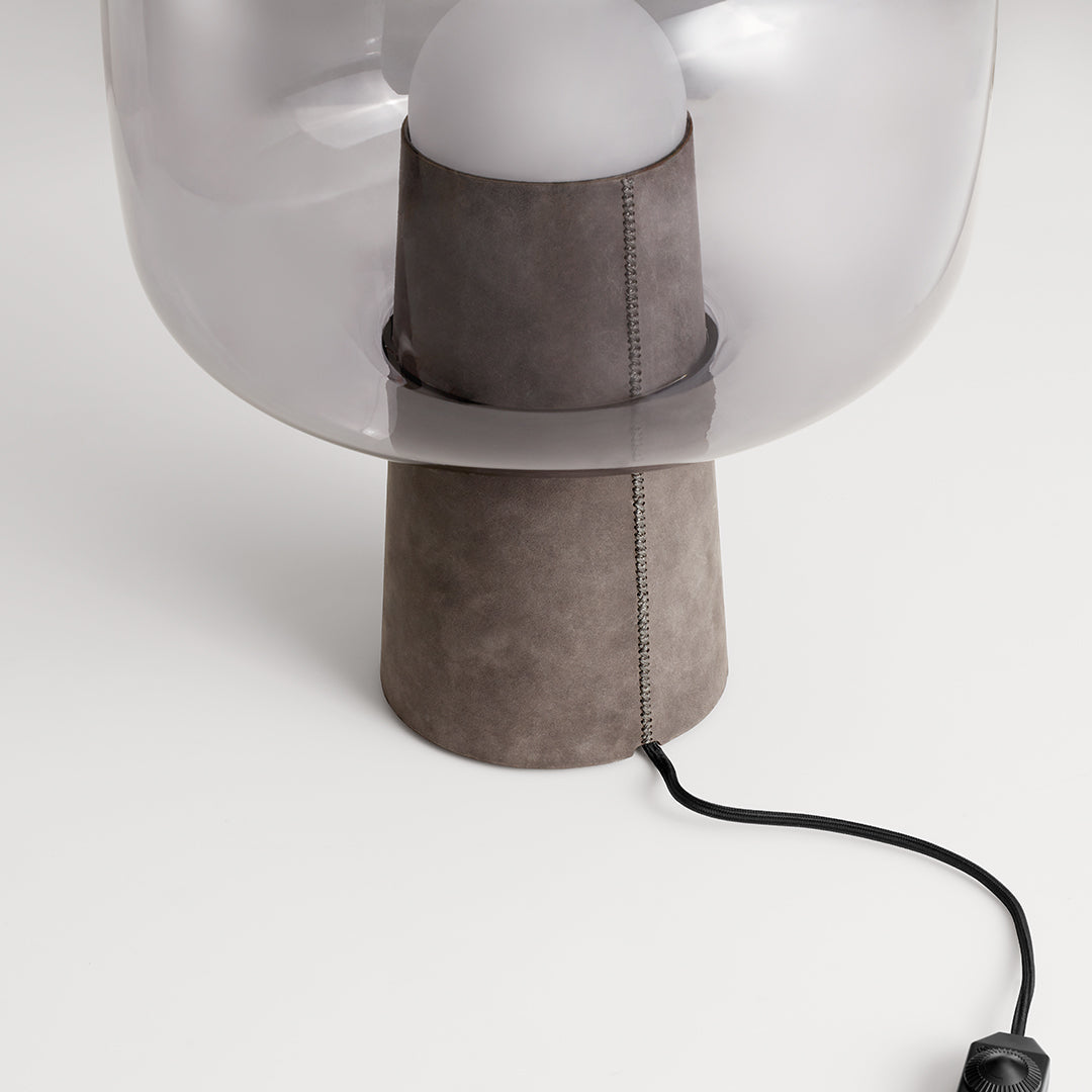 Transparent glass lamp with a gray suede base and black cord, showcasing a modern and minimalist design.