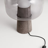 Transparent glass lamp with a gray suede base and black cord, showcasing a modern and minimalist design.