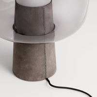 Gray suede lamp base with a translucent shade and sleek black cord, featuring a minimalist, modern design.