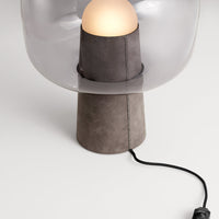 Gray lamp base with a clear shade and warm white spherical bulb, featuring a sleek contemporary design.