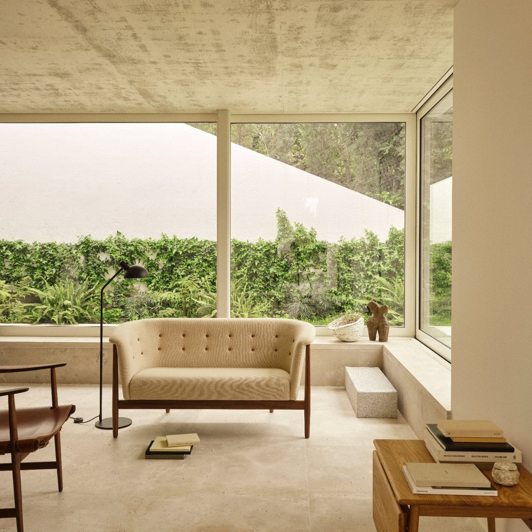 Beige tufted sofa with a minimalist design, set against a neutral background and greenery outside.