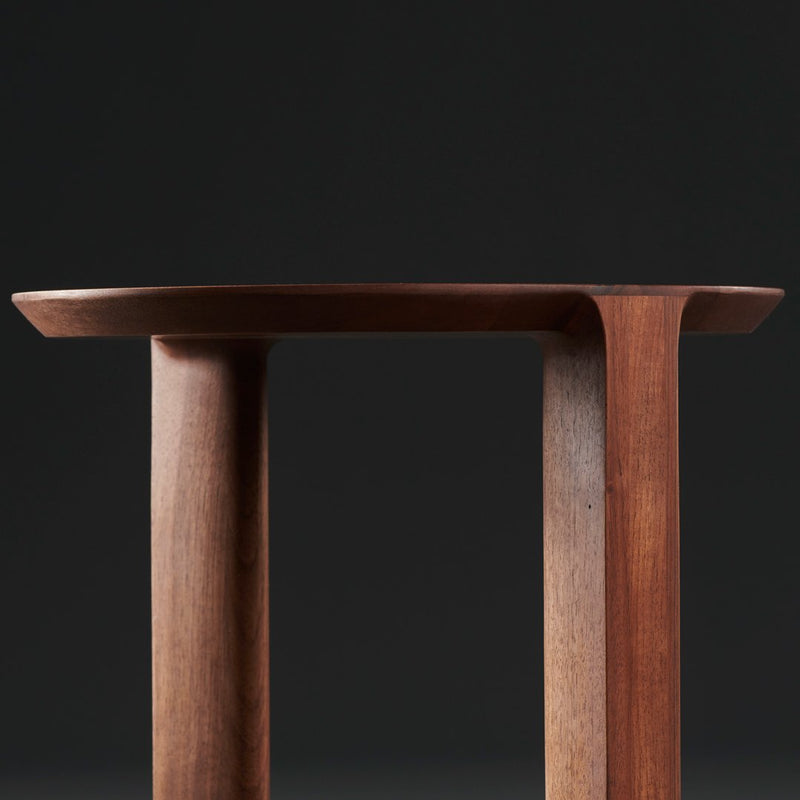 "Solid wood table with rich brown hues and smooth, minimalist design against a dark background."