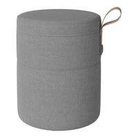 Round gray storage ottoman with a smooth texture and minimalist design, featuring a tan handle for easy carrying.