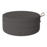 Gray circular pouf with a smooth fabric finish and a decorative handle. Modern, minimalist design.