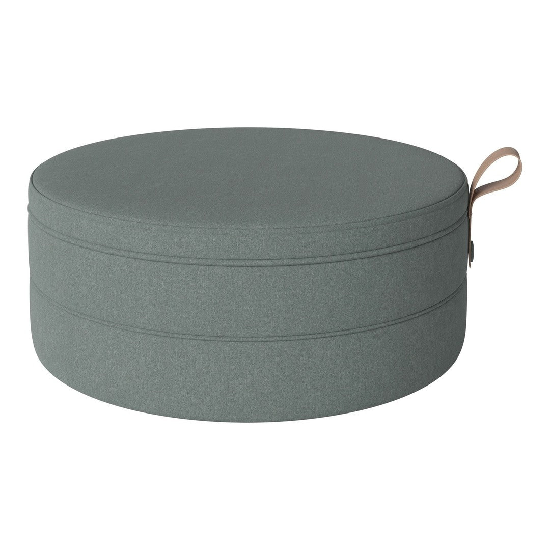 Round storage ottoman in soft grey fabric with a smooth texture and contrasting tan handle.