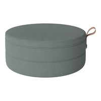 Round storage ottoman in soft grey fabric with a smooth texture and contrasting tan handle.