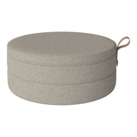 Round storage ottoman in soft taupe fabric with a smooth texture and minimalistic design. Ideal for modern decor.