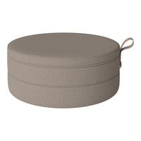 Round beige pouf with a textured fabric and a stylish handle for easy portability. Perfect for modern decor.