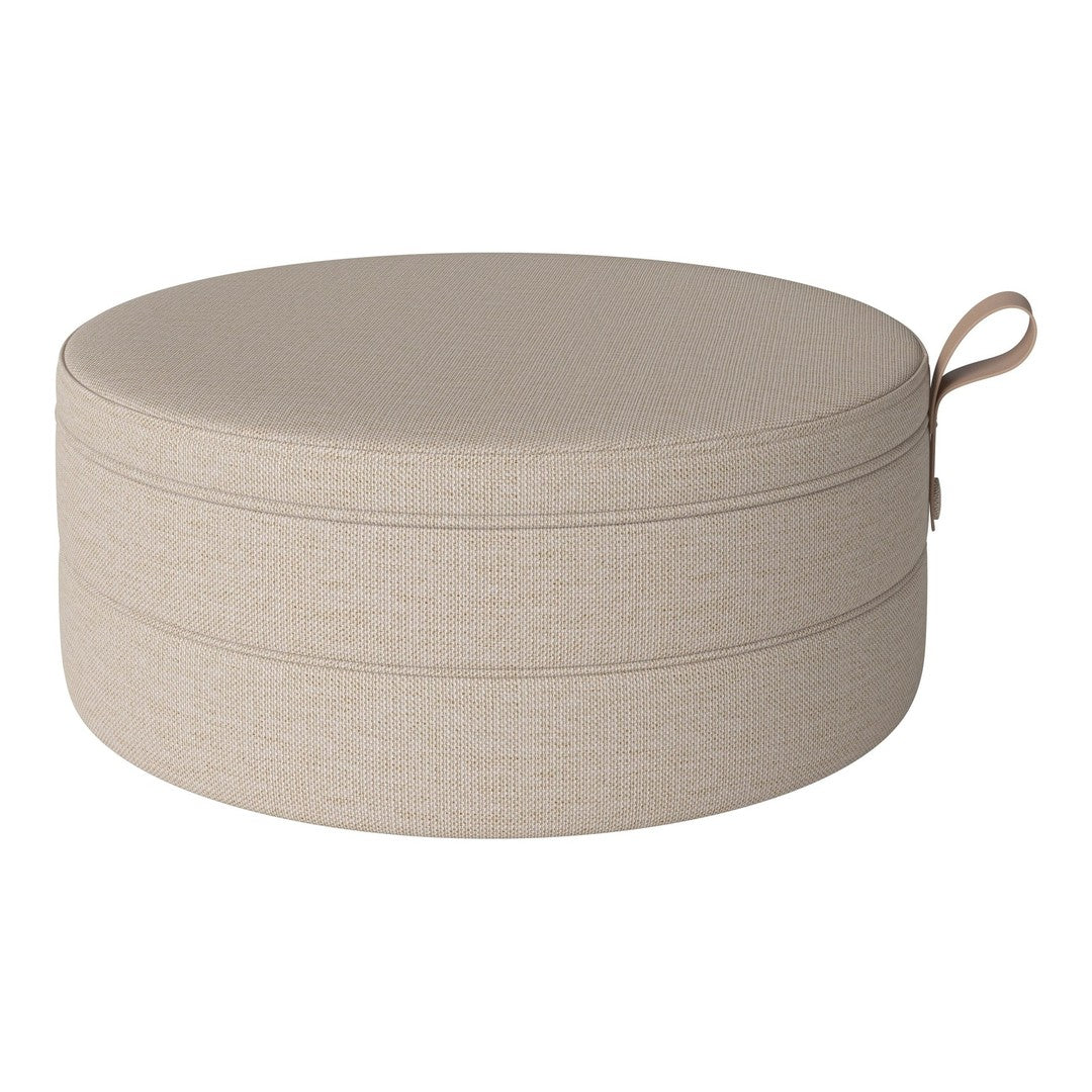 Round storage ottoman in soft beige fabric with a subtle textured pattern and convenient carry handle.