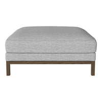 Gray upholstered ottoman with a smooth texture and brown wooden legs, perfect for modern decor.