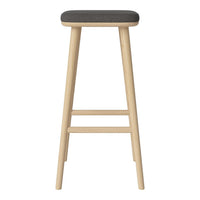 Minimalist wooden bar stool with a light natural finish and a dark gray upholstered seat. Simple, modern design.