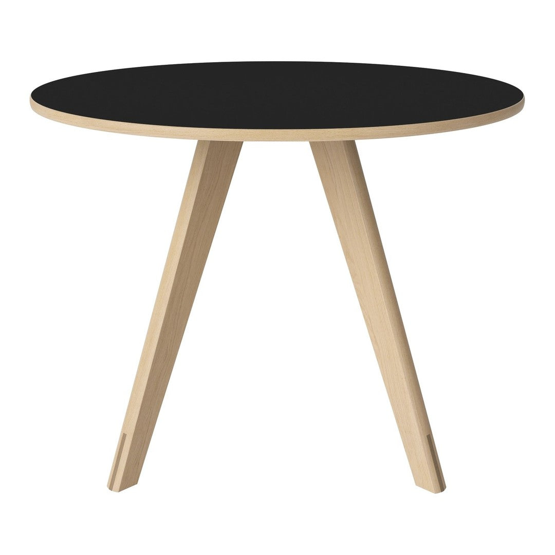 Round black table with natural wood legs, showcasing a minimalist design and contrasting colors. Perfect for modern decor.