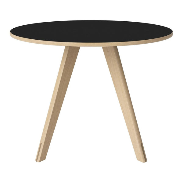 Round black table with natural wood legs, showcasing a minimalist design and contrasting colors. Perfect for modern decor.