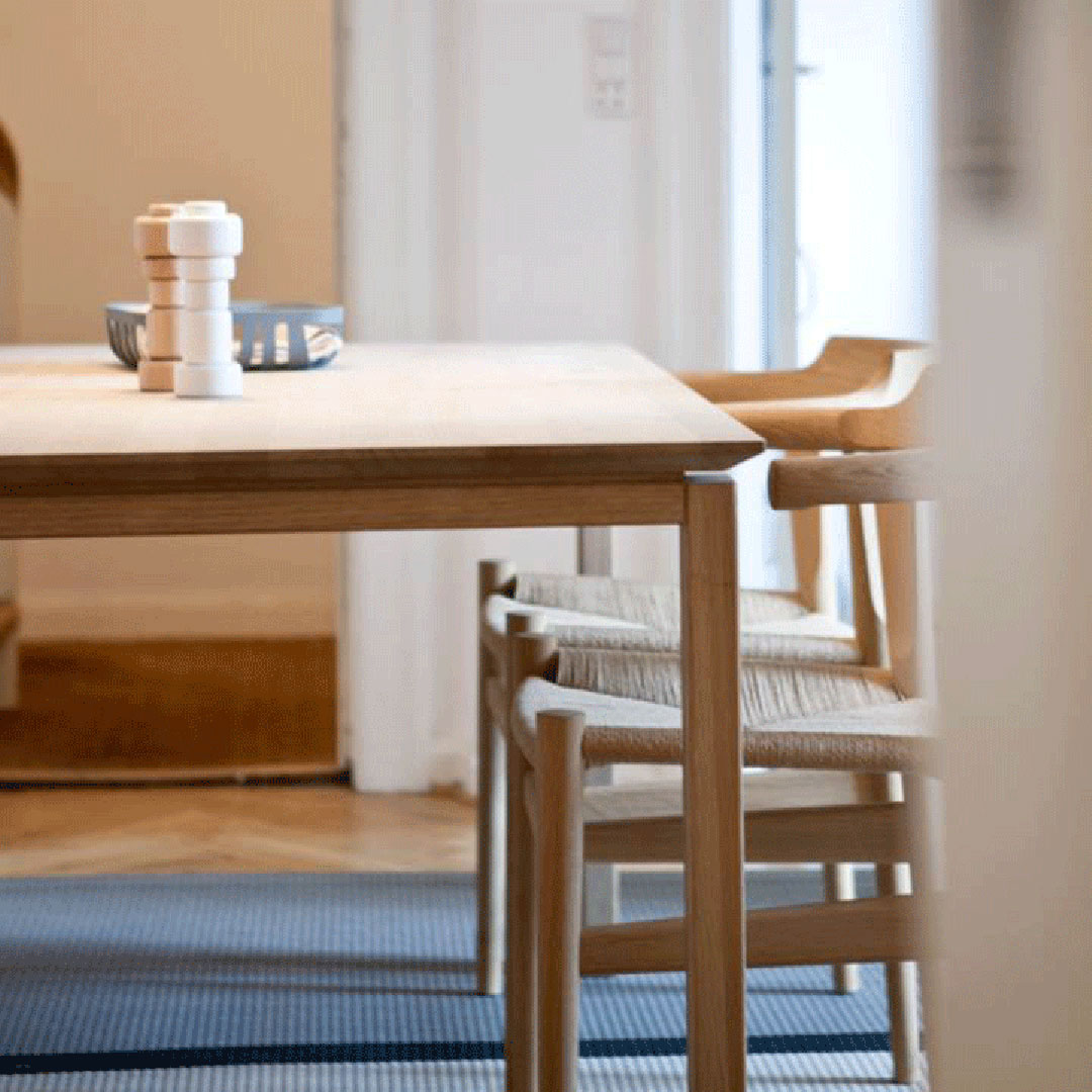 Light oak dining table with natural wood chairs and a soft blue patterned rug, enhancing a minimalist aesthetic.