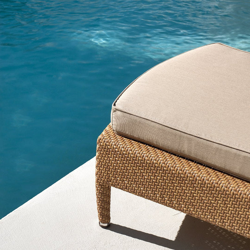 Beige cushion on woven tan wicker chair by a serene blue pool, creating a stylish outdoor vibe.