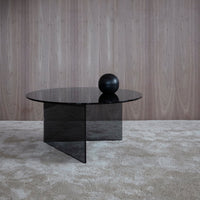 Elegant black round coffee table with sleek glass surface and minimalist geometric design on a neutral beige rug.