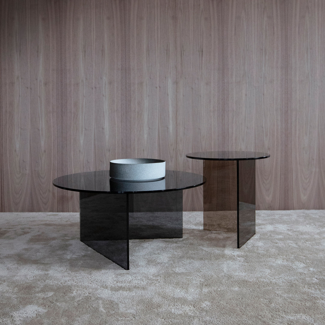 Black glass coffee tables with smooth, round tops and sleek geometric bases against a textured beige rug.
