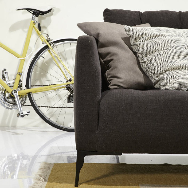 Dark brown sofa with textured gray and beige pillows, complemented by a yellow bicycle in a bright, modern setting.