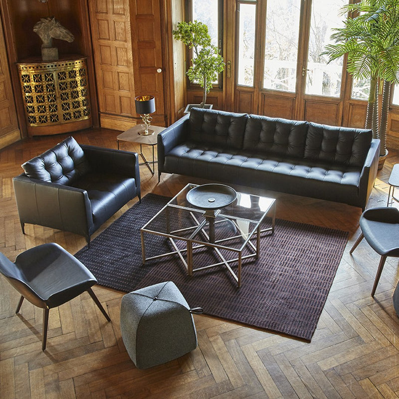 Sleek black leather furniture with tufted detailing and a geometric glass table on a dark textured rug.