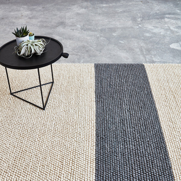 Beige and dark gray striped area rug on a textured surface, complementing modern decor.