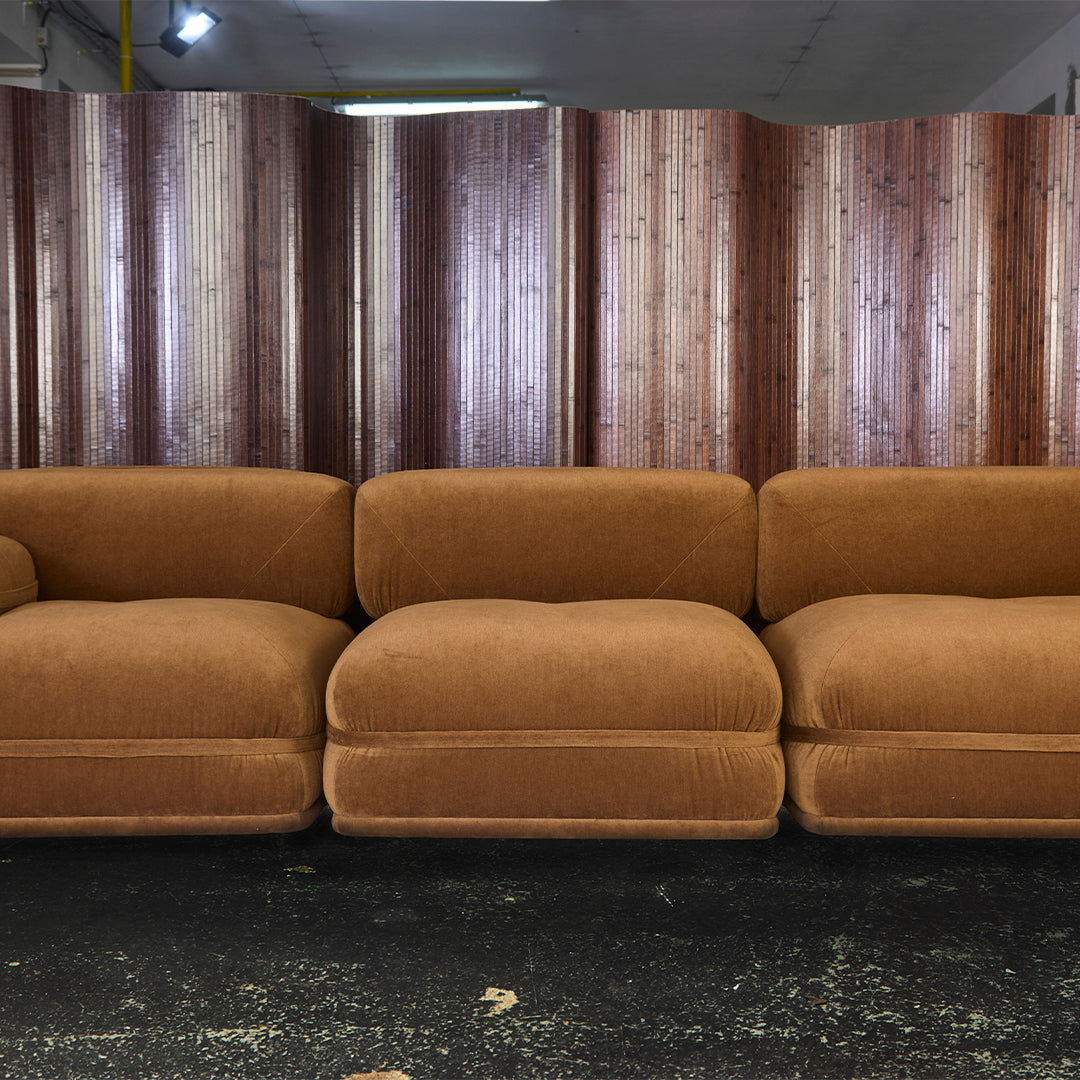 "Rust-colored corduroy sectional sofa with plush, oversized cushions against a wooden backdrop."