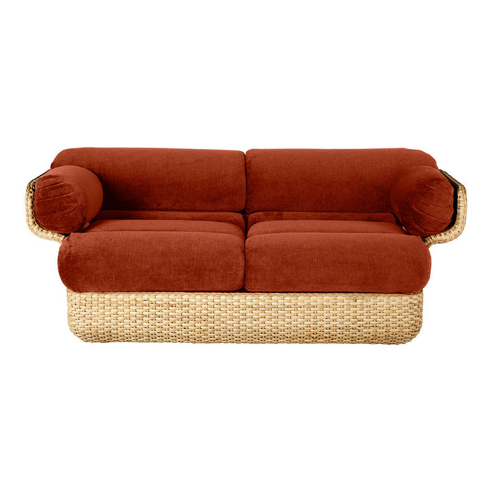 Rust-colored plush cushions on a woven natural rattan base, featuring rounded armrests for a cozy aesthetic.